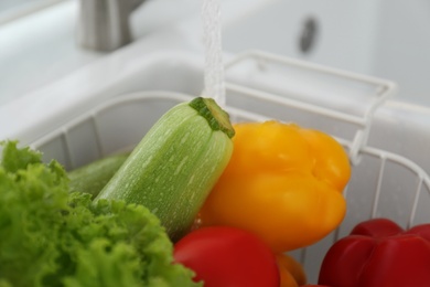 Photo of Many fresh ripe vegetables under tap water in kitchen sink, closeup