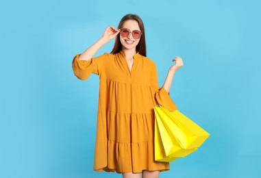 Photo of Happy young woman with shopping bags on light blue background. Big sale