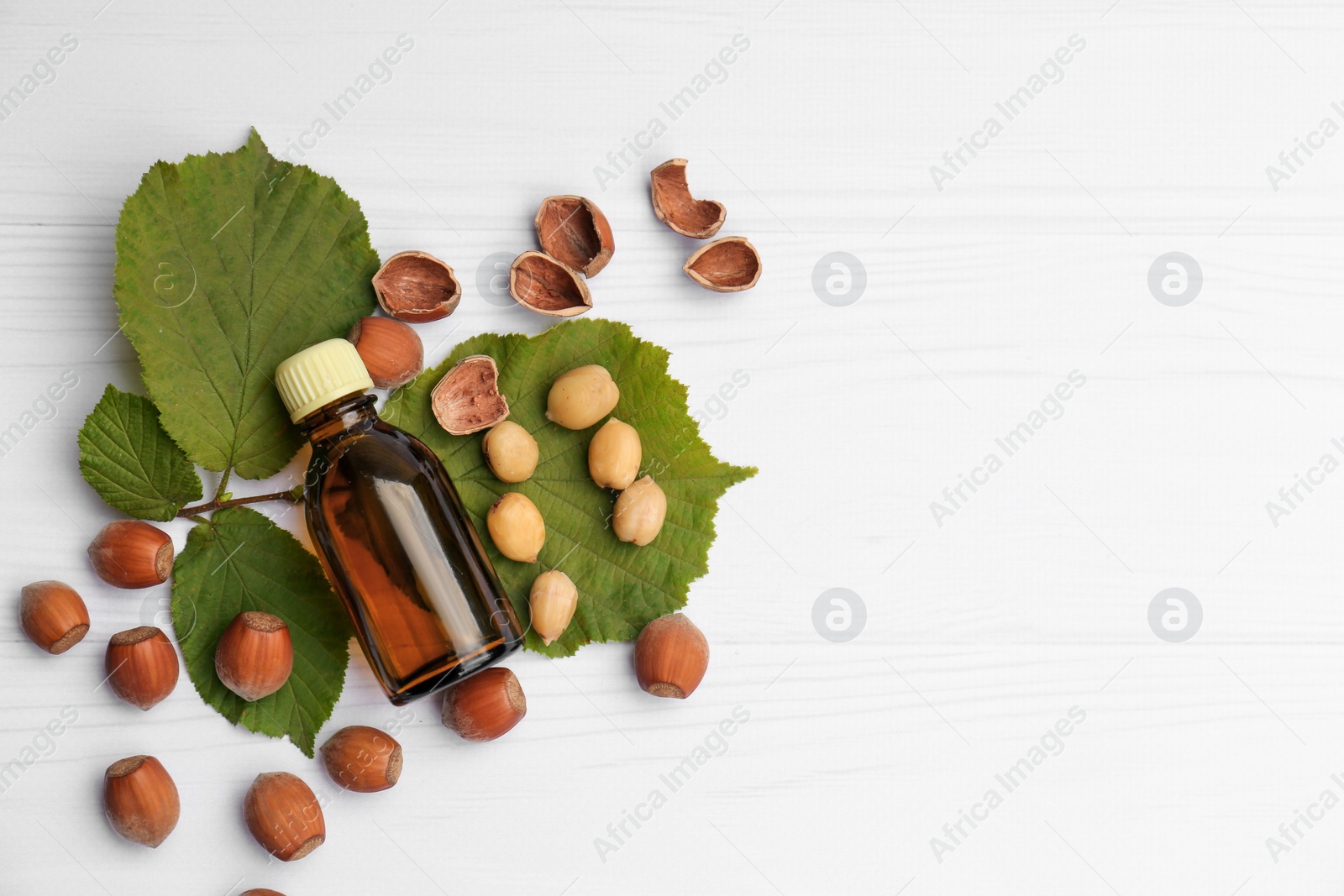 Photo of Bottle of hazelnut essential oil and nuts on white wooden table, flat lay. Space for text