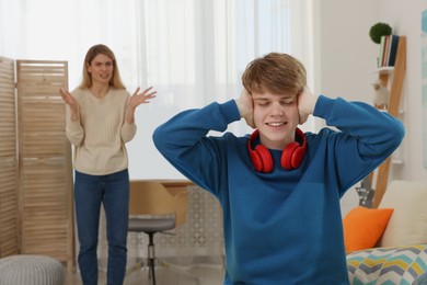 Teenage son covering his ears and ignoring mother while she scolding him at home