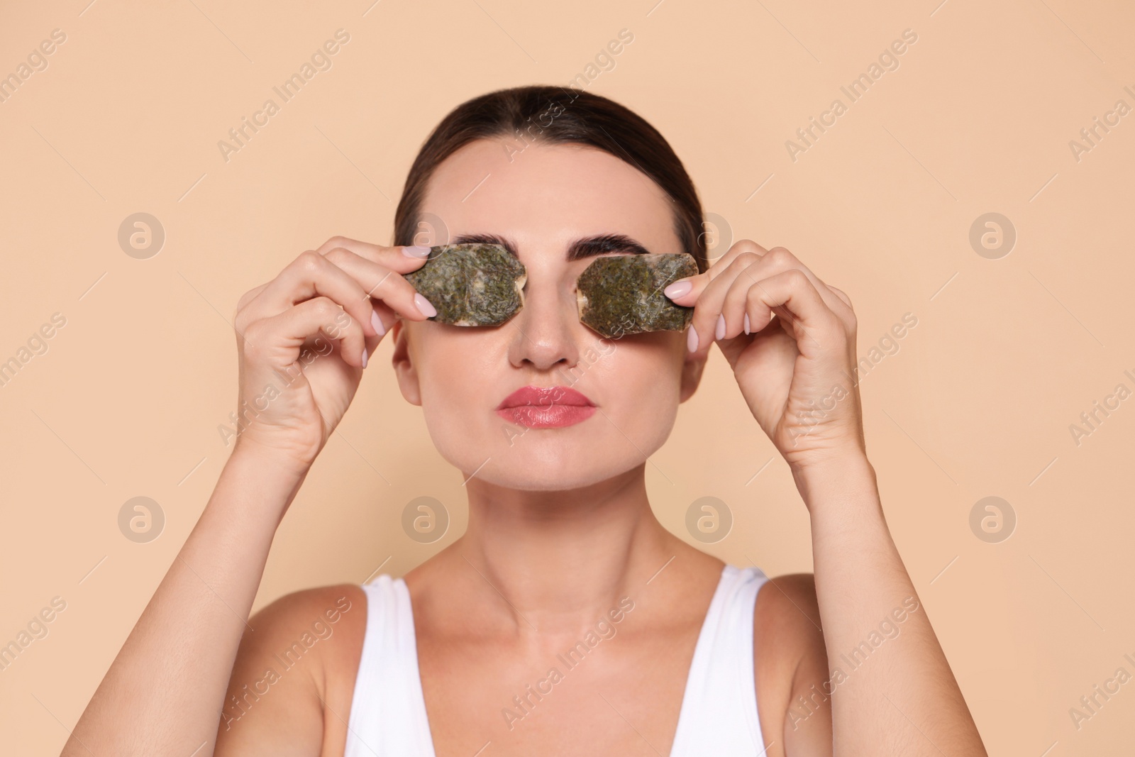 Photo of Beautiful woman applying green tea bags on skin under eyes against beige background