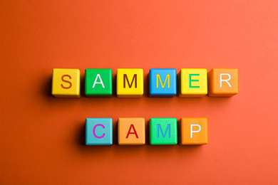 Colorful wooden cubes with phrase SUMMER CAMP on red background, flat lay
