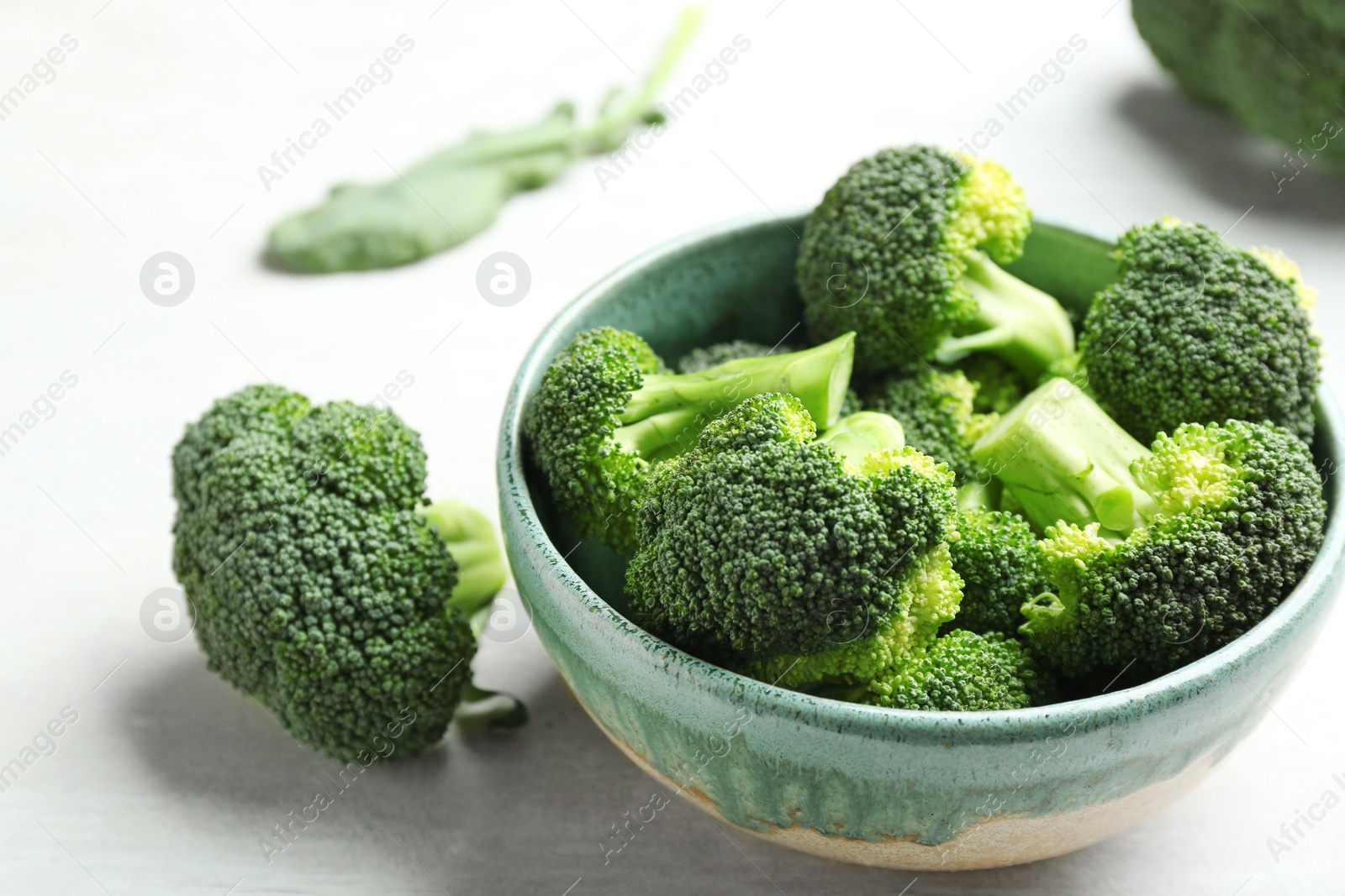 Photo of Bowl and fresh broccoli on light grey table, closeup