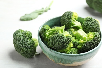 Photo of Bowl and fresh broccoli on light grey table, closeup