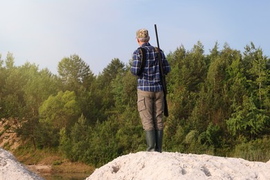 Man with hunting rifle near forest outdoors, back view