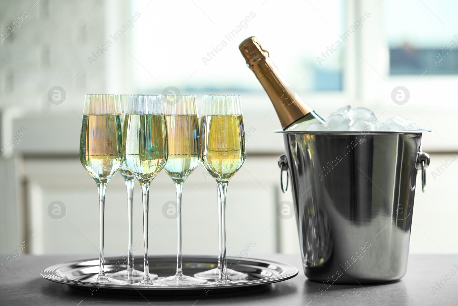 Photo of Glasses of champagne and ice bucket with bottle on grey table