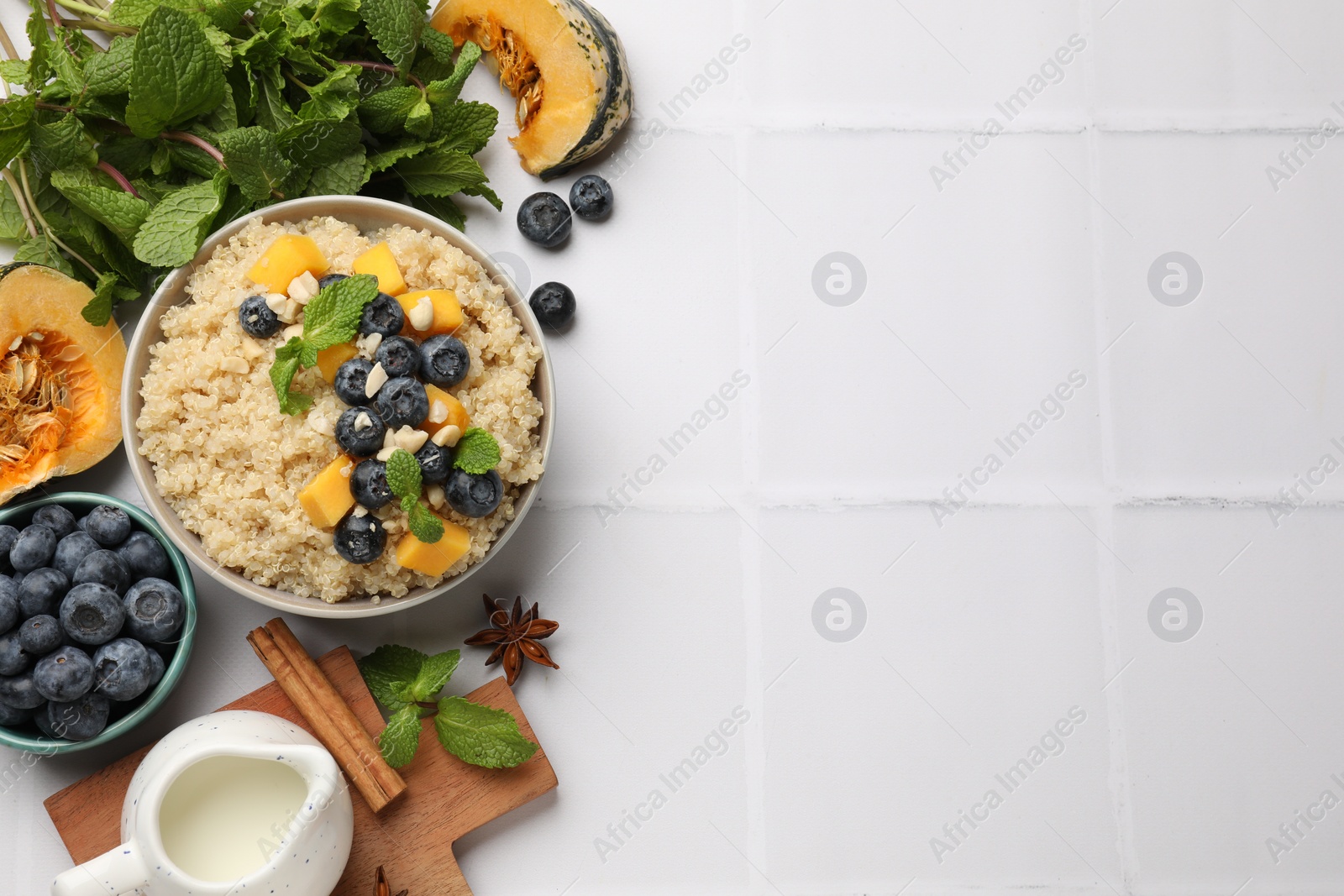 Photo of Flat lay composition with bowl of tasty quinoa porridge, blueberries and pumpkin on white tiled table. Space for text