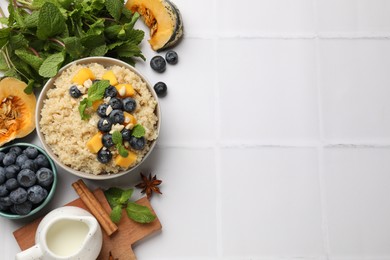 Flat lay composition with bowl of tasty quinoa porridge, blueberries and pumpkin on white tiled table. Space for text