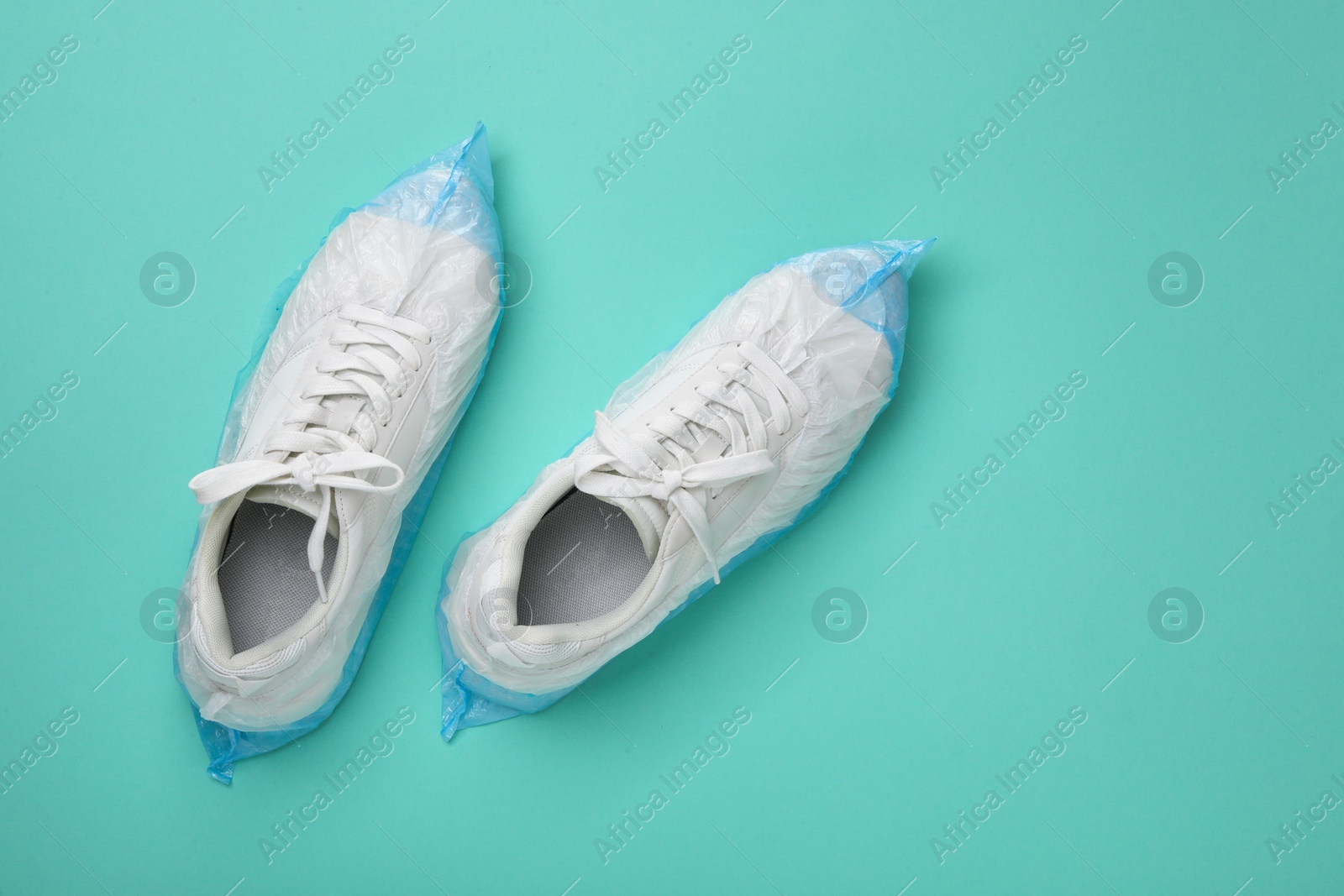 Photo of Sneakers in shoe covers on turquoise background, top view. Space for text