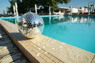 Photo of Shiny disco ball on edge of swimming pool. Party decor