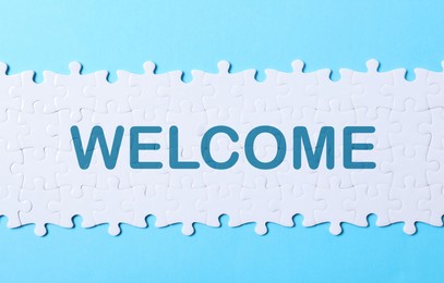 Image of White puzzle pieces and word WELCOME on light blue background, top view