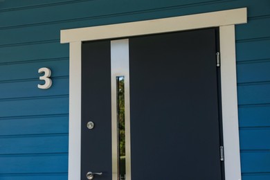 Photo of Number three on blue wooden house near stylish door outdoors