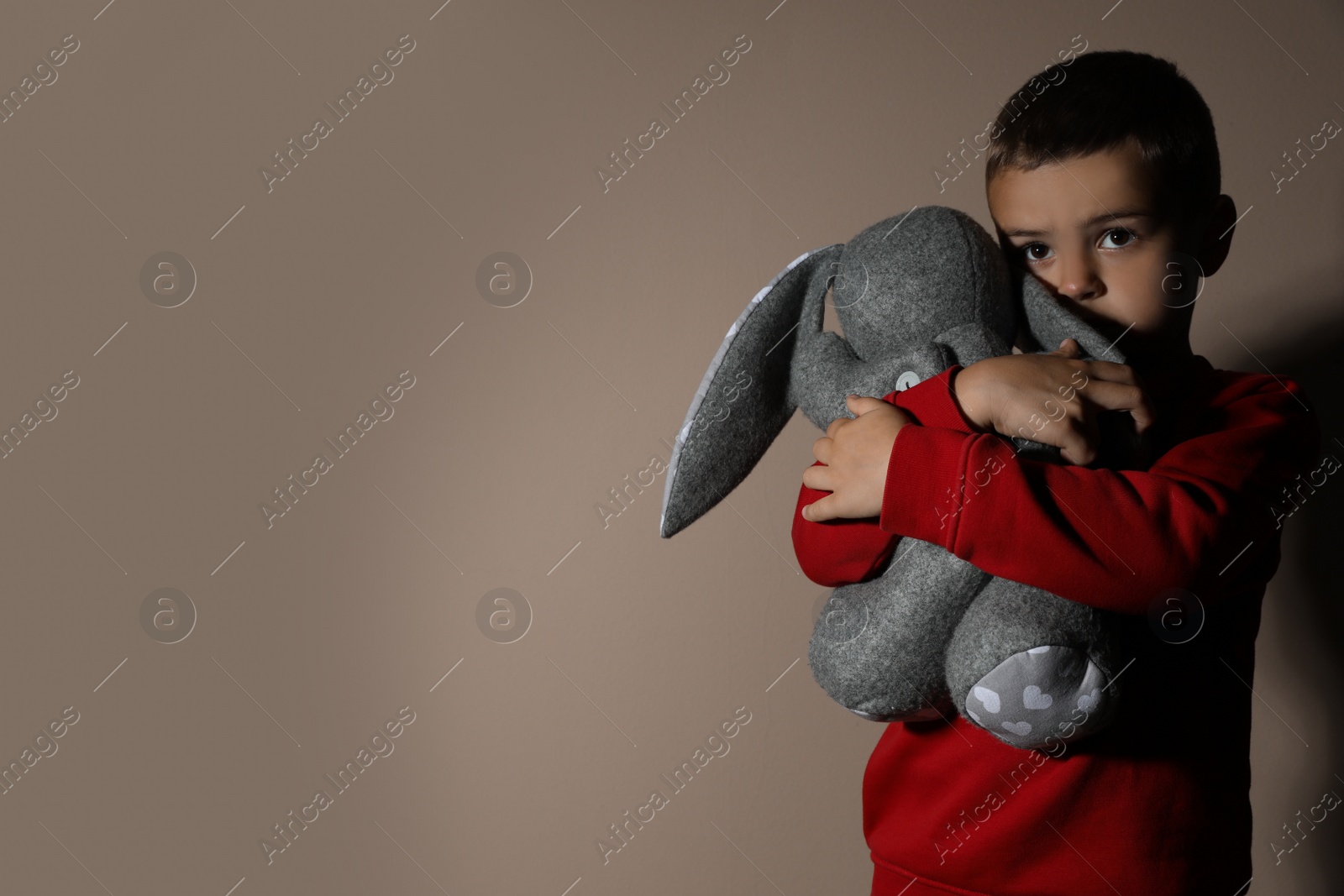 Photo of Sad little boy with toy on beige background, space for text. Domestic violence concept