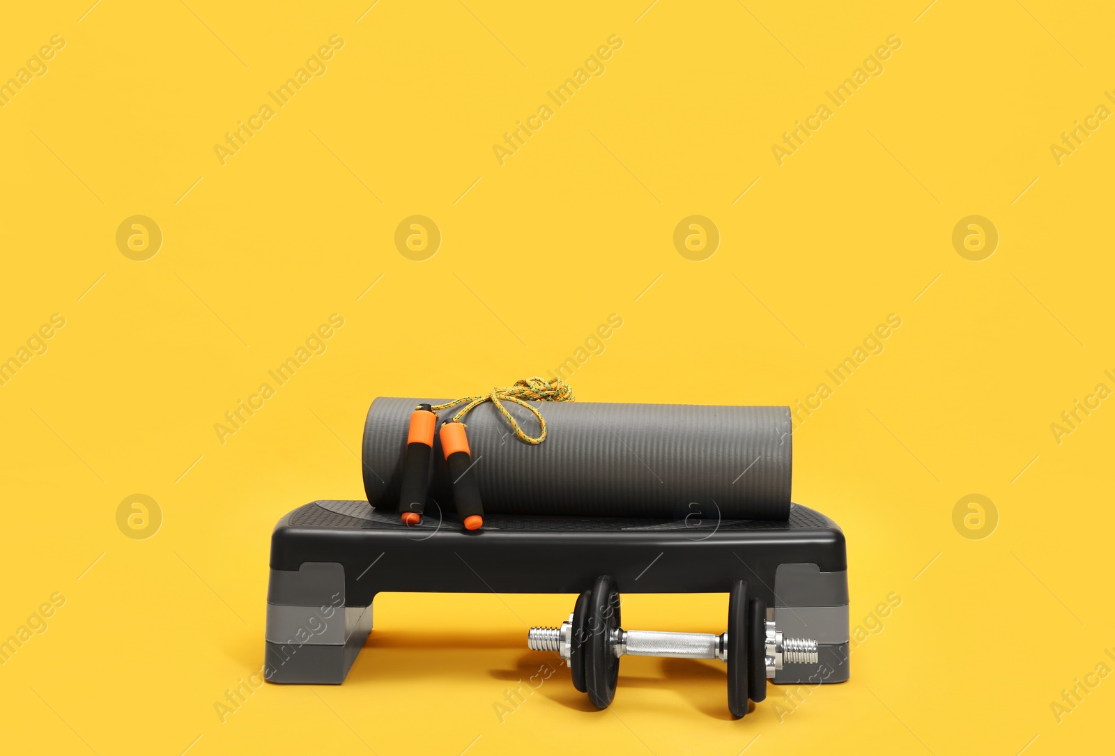 Photo of Step platform, dumbbell, mat and jump rope on yellow background. Sports equipment