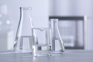 Photo of Different laboratory glassware with transparent liquid on wooden table against blurred background. Space for text