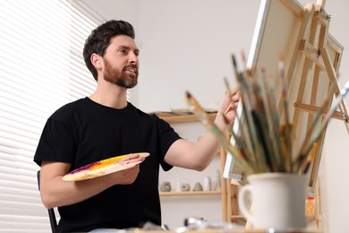 Photo of Man painting in studio. Using easel to hold canvas