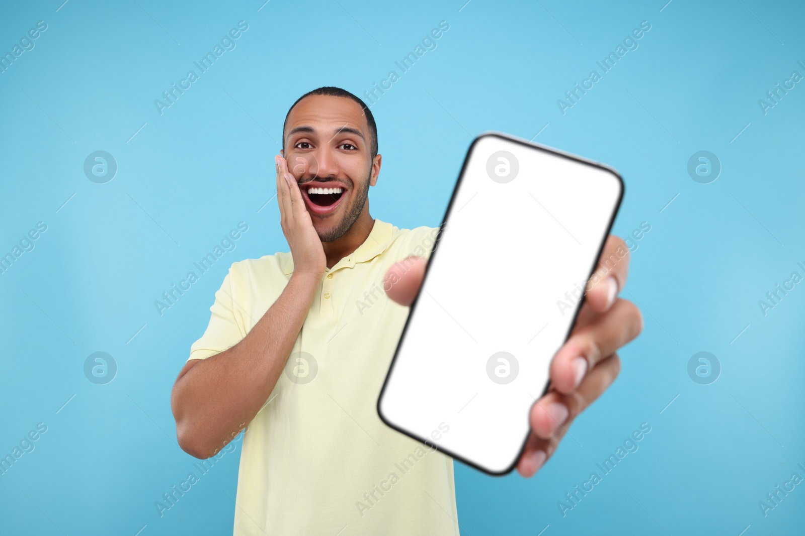 Photo of Surprised man showing smartphone in hand on light blue background