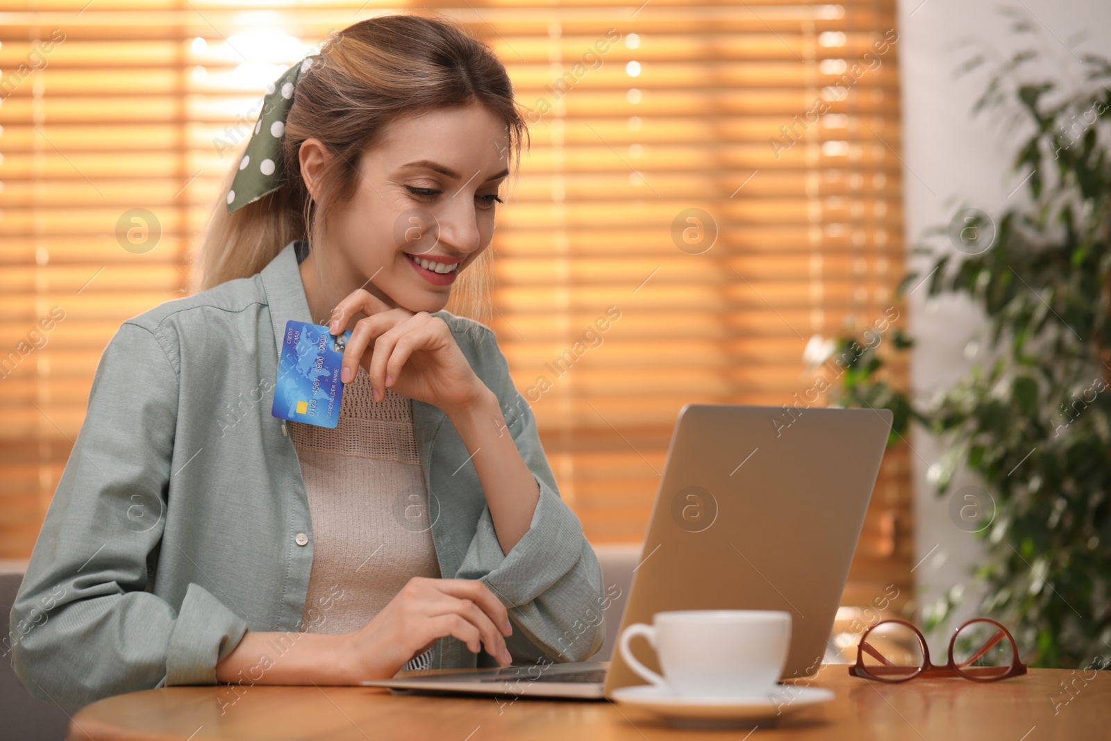 Photo of Woman with credit card using laptop for online shopping at wooden table indoors