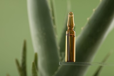 Skincare ampoule near aloe vera on light green background, closeup