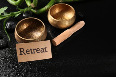 Photo of Card with word Retreat, singing bowls, spa stones and bamboo stems on wet black table. Space for text