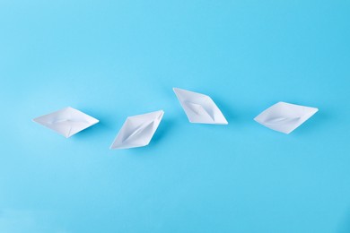 Photo of Handmade white paper boats on light blue, flat lay. background. Origami art