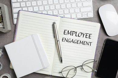 Image of Notebook with text EMPLOYEE ENGAGEMENT, smartphone and stationery on grey table, flat lay