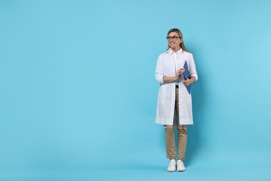 Photo of Portrait of happy doctor with clipboard on light blue background, space for text