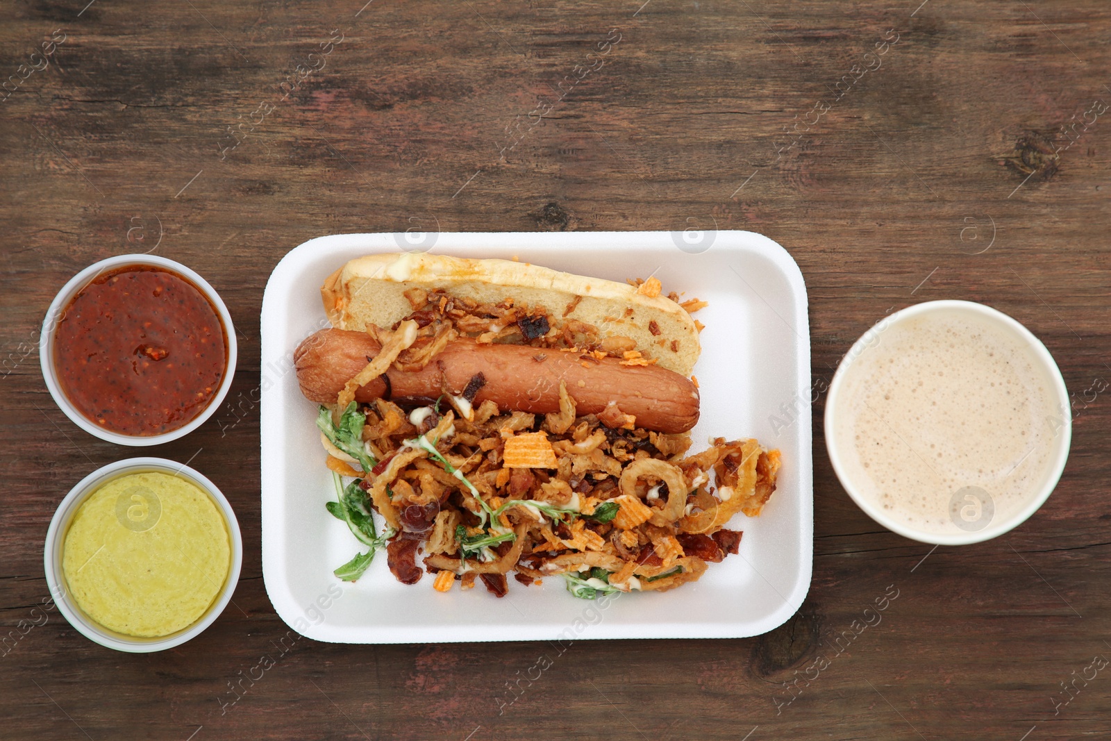 Photo of Fresh delicious hot dog with sauces and paper cup of coffee on wooden table, flat lay