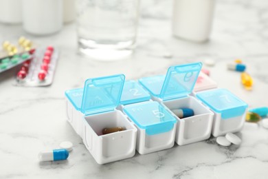 Photo of Plastic box with different pills on white marble table