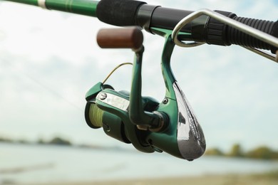 Photo of Fishing rod with reel near river, closeup