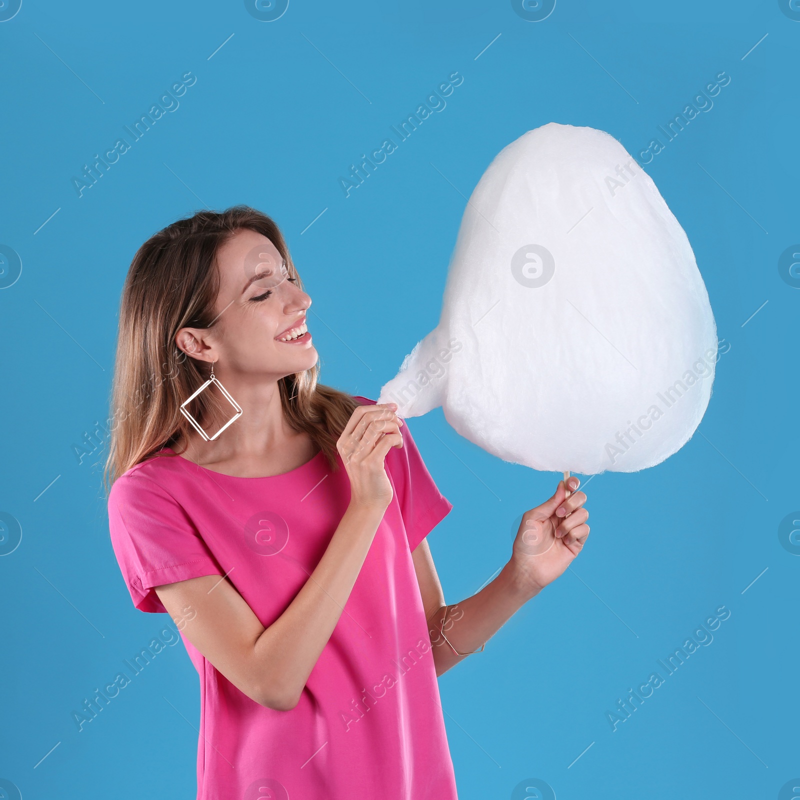 Photo of Happy young woman eating cotton candy on blue background