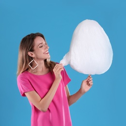 Photo of Happy young woman eating cotton candy on blue background