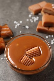Photo of Tasty salted caramel with candies in glass bowl on grey table
