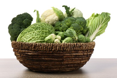 Photo of Wicker bowl with different types of fresh cabbage on wooden table against white background