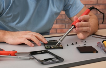 Technician repairing broken smartphone at table, closeup