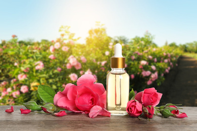 Bottle of rose essential oil and flowers on wooden table against blurred background