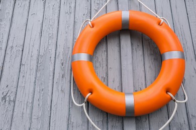 Photo of Orange life buoy hanging on light wooden wall, space for text