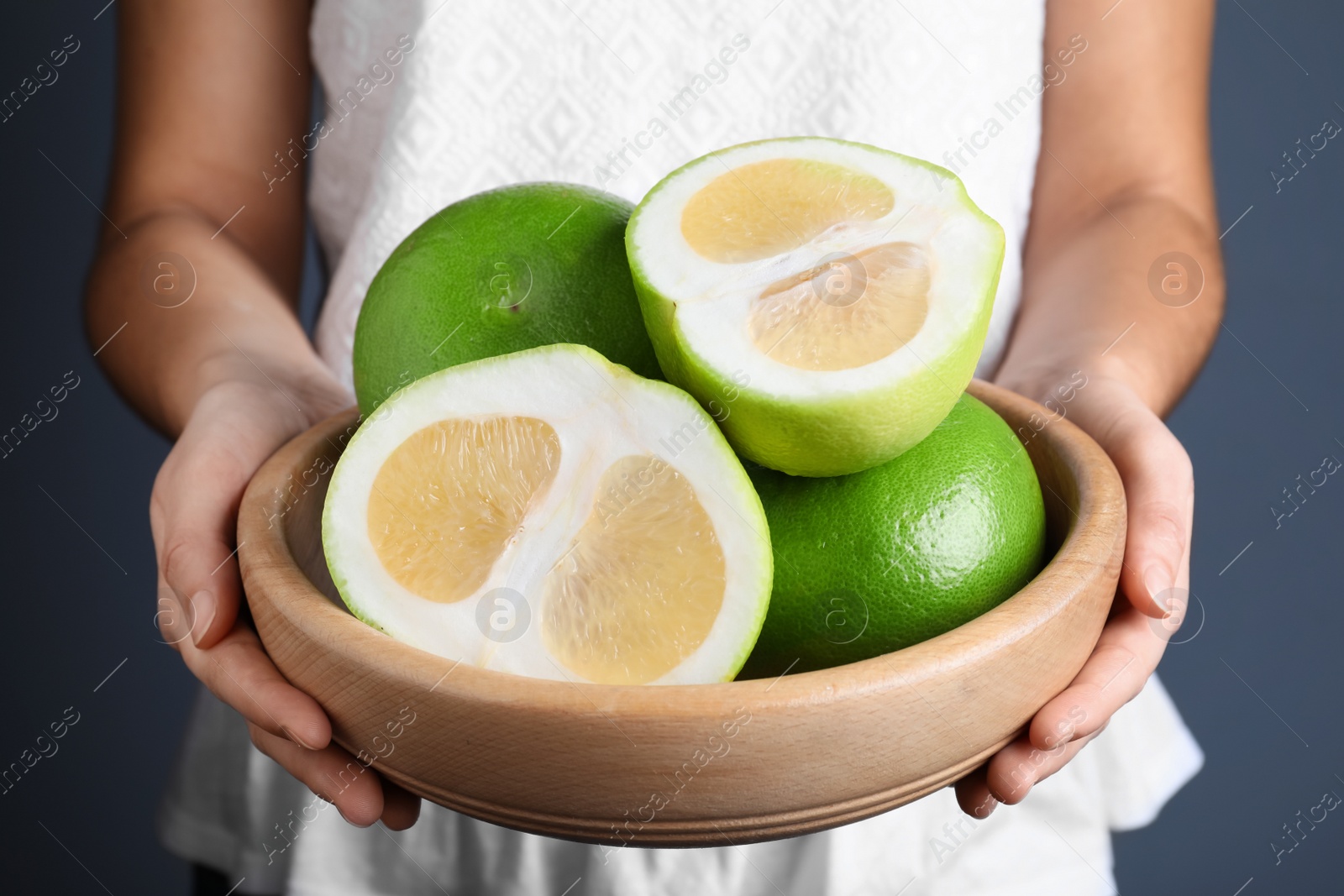 Photo of Woman holding bowl with sweetie fruits on blue background, closeup