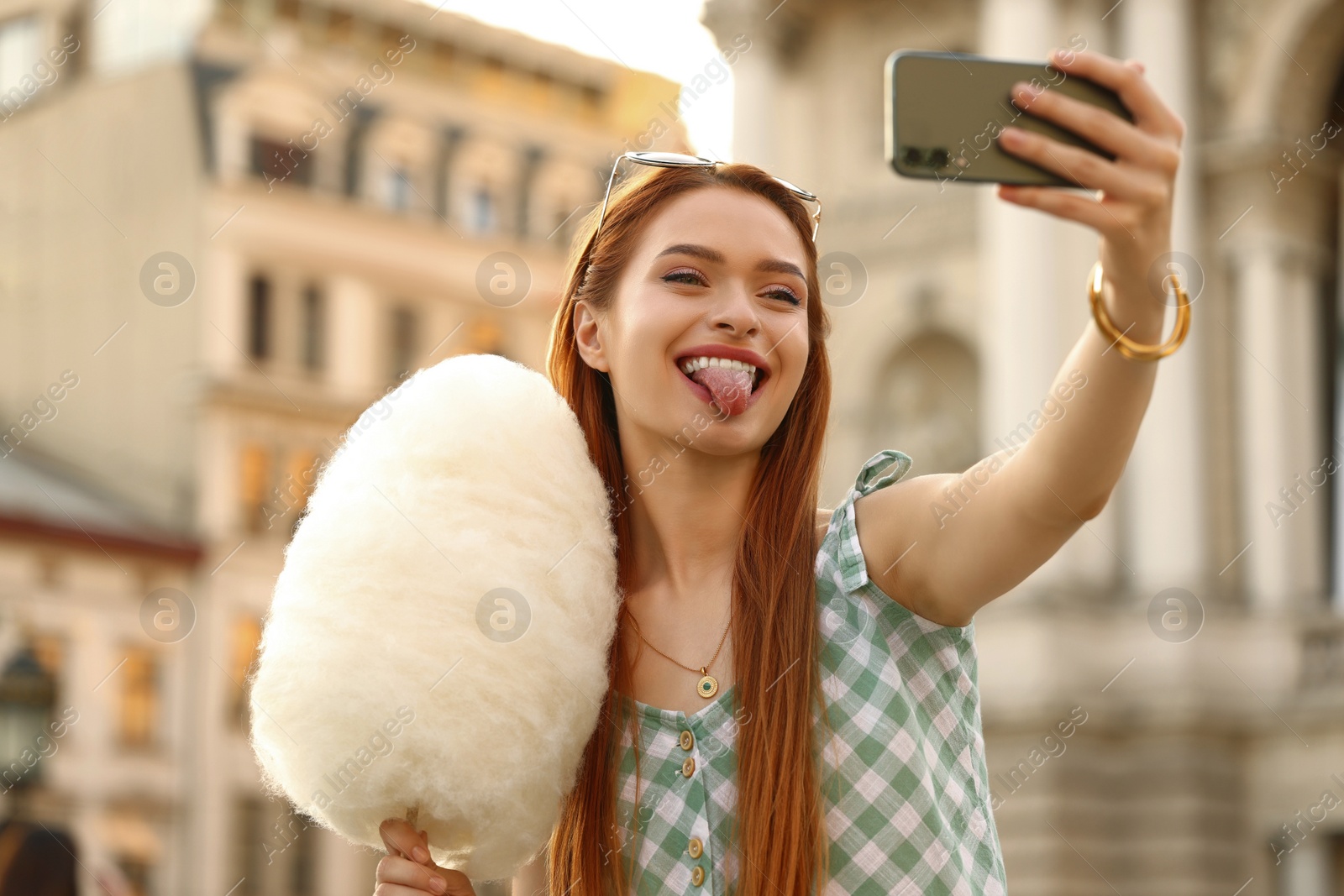 Photo of Smiling woman with cotton candy taking selfie on city street