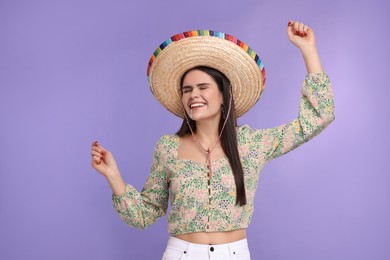 Young woman in Mexican sombrero hat dancing on violet background