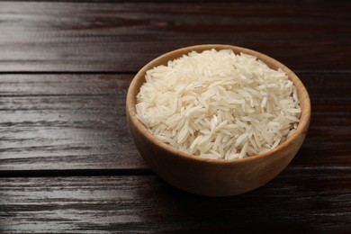 Photo of Raw basmati rice in bowl on wooden table, space for text