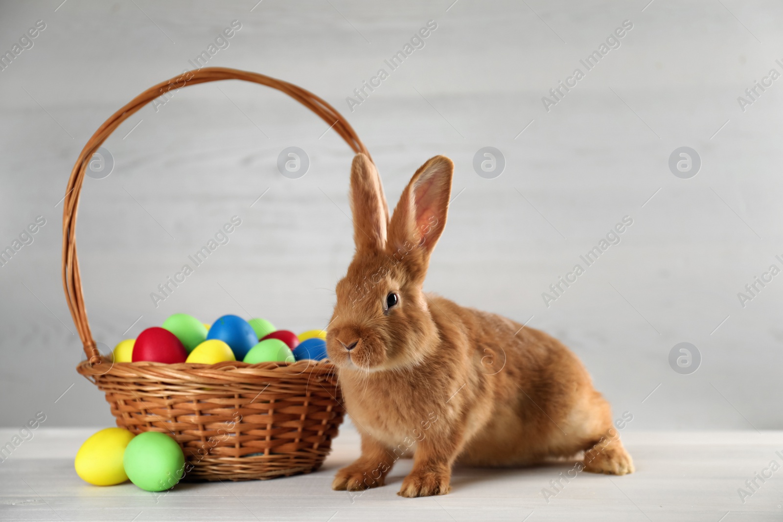 Photo of Cute bunny and basket with Easter eggs on white table