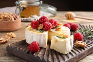 Photo of Brie cheese served with raspberries, walnuts and honey on wooden table, closeup
