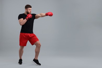 Photo of Man in boxing gloves fighting on grey background. Space for text