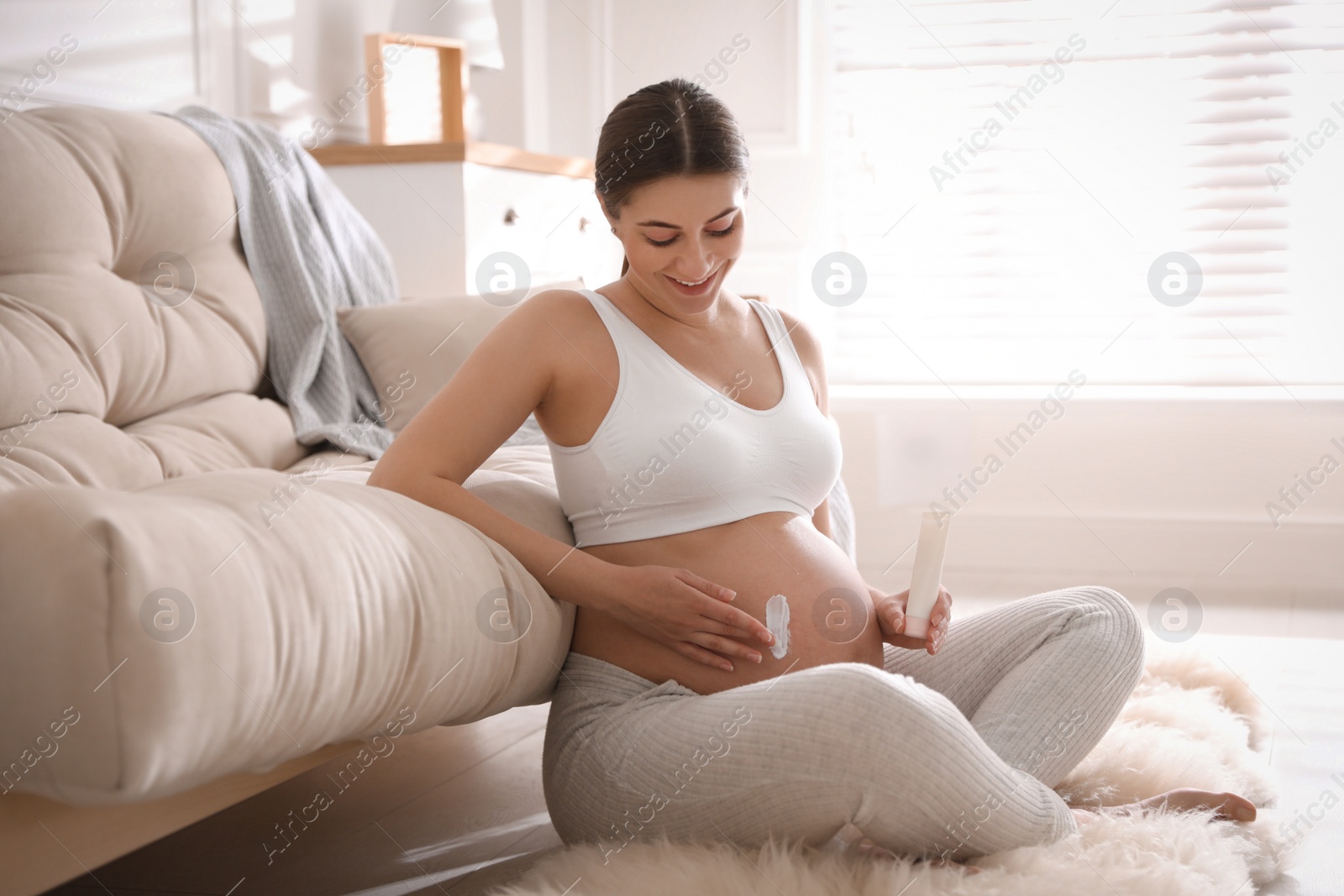 Photo of Young pregnant woman with cosmetic product at home