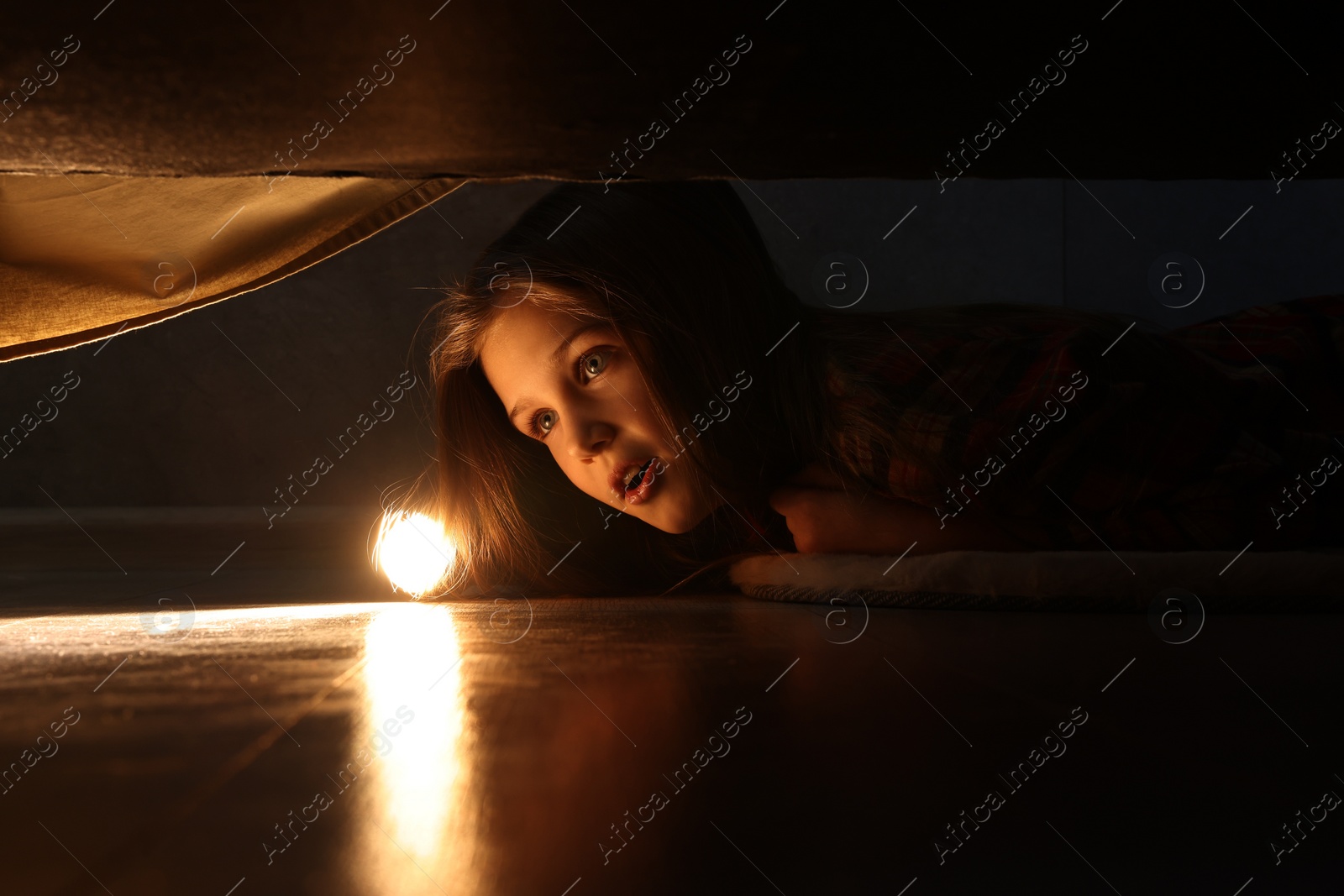 Photo of Little girl with flashlight looking for monster under bed at night