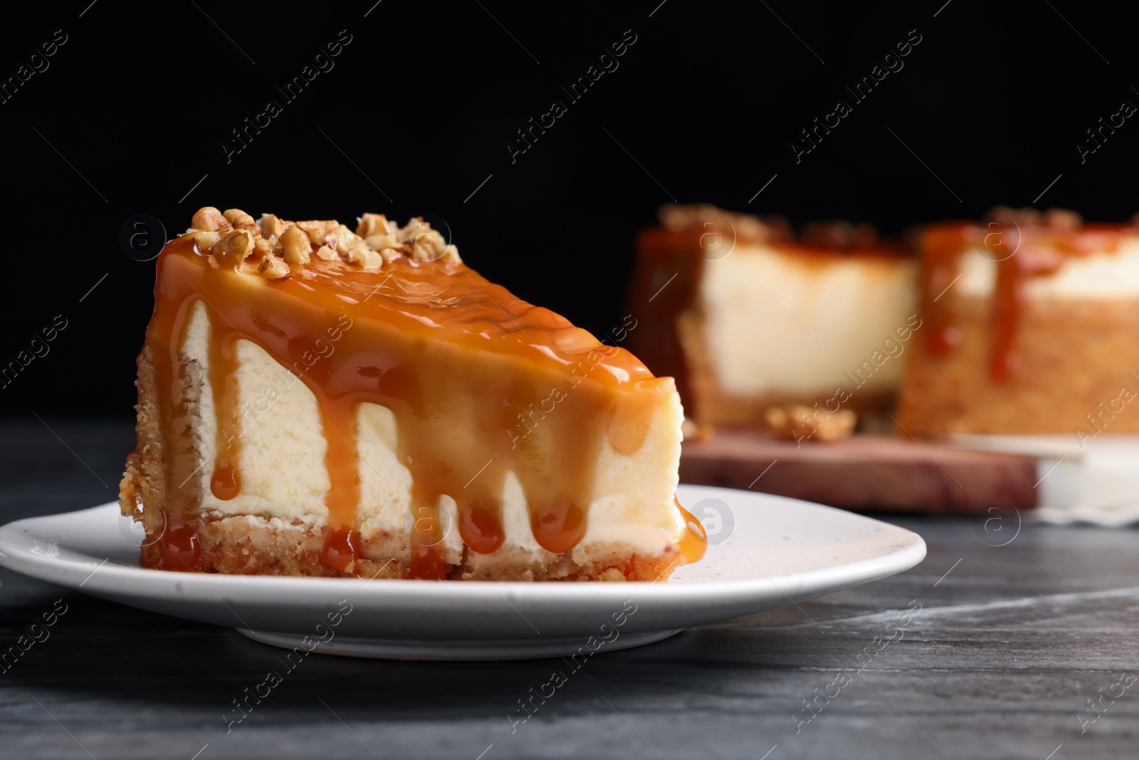 Photo of Piece of delicious cake with caramel and walnuts on black marble table, space for text