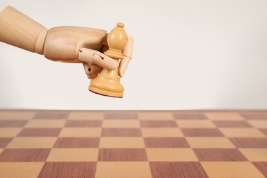 Photo of Robot with chess piece above board against light background, space for text. Wooden hand representing artificial intelligence