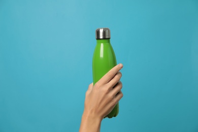 Photo of Woman holding modern green thermos on light blue background, closeup