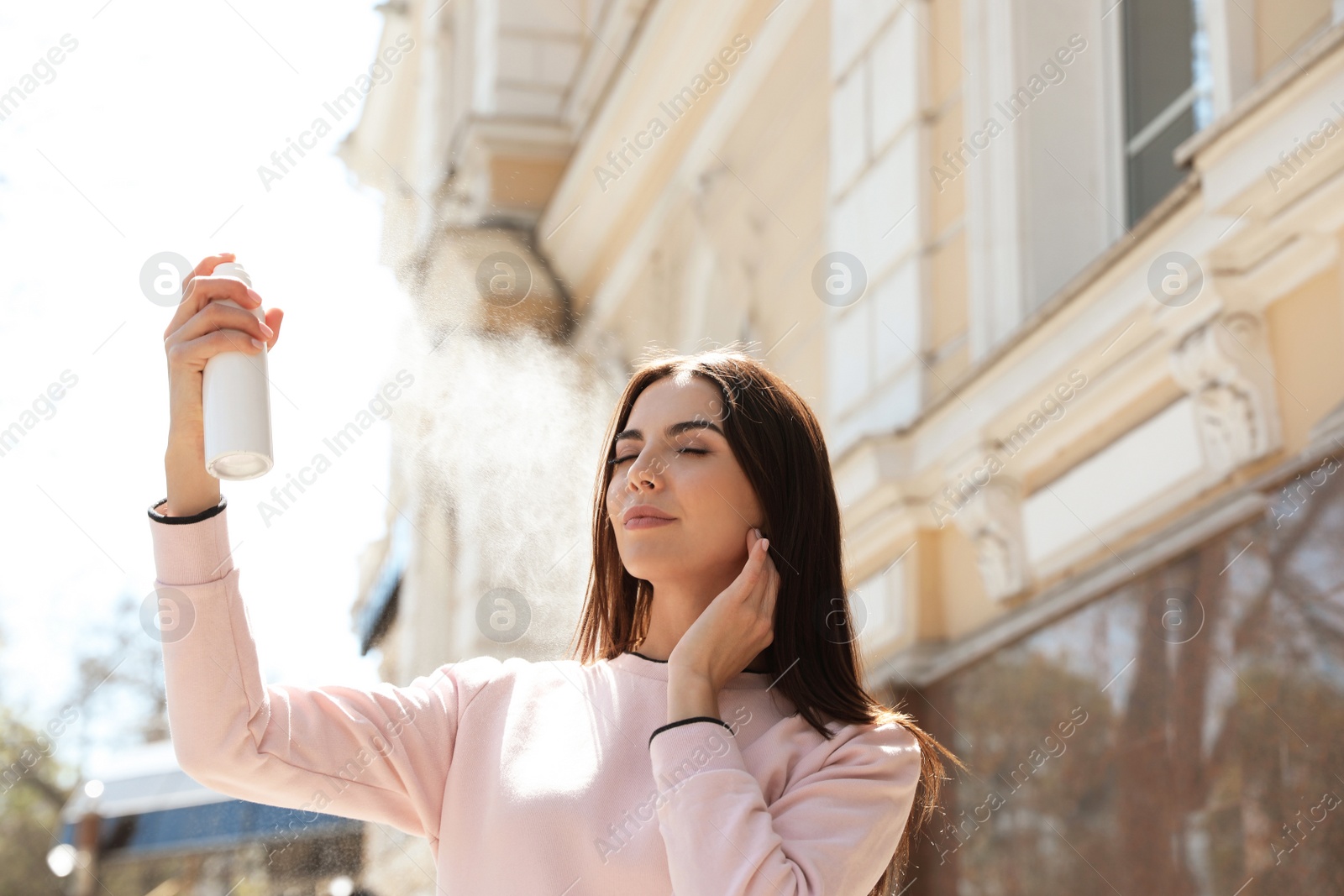 Photo of Young woman applying thermal water on face outdoors, space for text. Cosmetic product